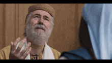 a man with a beard wearing a hat talks to another man