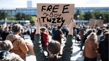 a woman is holding a sign that says `` free my boy twizzly '' .