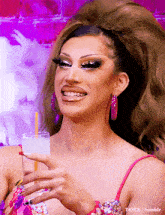 a drag queen is holding a drink with a straw and smiling