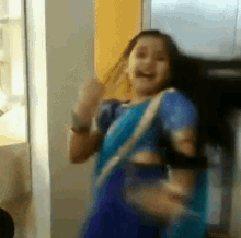 a woman in a blue saree is dancing in a room with her mouth open .