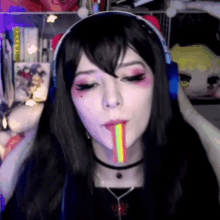 a woman wearing headphones and a choker is sticking out a rainbow colored lollipop .