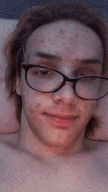 a shirtless man wearing glasses and earrings smiles for the camera
