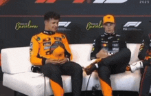 two racing drivers are sitting on a couch holding a hat .