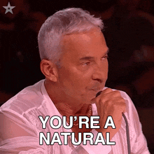 a man singing into a microphone with the words " you 're a natural " above him