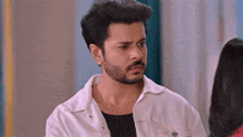 a man with a beard is wearing a white jacket and looking at a woman .