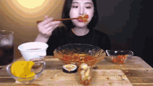 a woman is eating a bowl of food with chopsticks while sitting at a table