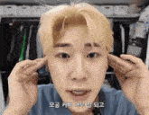 a young man with blonde hair is covering his ears with his hands in a closet .