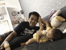 a man is feeding a baby from a bottle while laying on a couch with stuffed animals