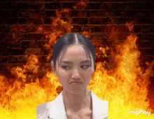 a woman is making a funny face in front of a brick wall with fire behind her