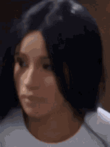 a close up of a woman 's face with long black hair and a white shirt .