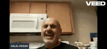 a bald man with a beard is smiling in front of a microwave with the name halal hogan on the screen