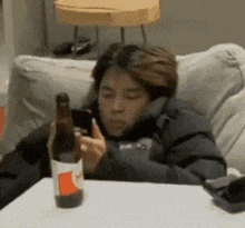 a person is sitting on a couch holding a bottle of beer and looking at their phone .