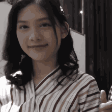 a woman wearing a striped shirt is smiling and giving a thumbs up