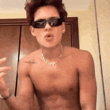 a shirtless young man wearing sunglasses and a necklace is making a funny face .