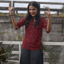 a woman wearing a red top and black pants stands in front of a fence with the words sanjo sebi on the bottom right
