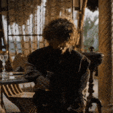 a man with curly hair sits at a table holding a pitcher and a glass