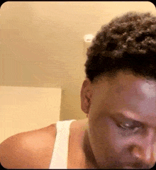 a man in a white tank top is looking down at something .