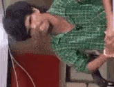 a man in a green plaid shirt is laying on his back on a table .