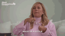a woman wearing a pink sweater with pearls on the sleeves says back up a little