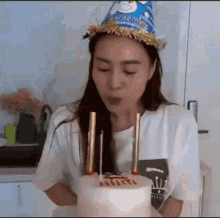 a woman is blowing out candles on a birthday cake while wearing a party hat .