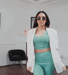 a woman wearing sunglasses and a white jacket is walking in a room
