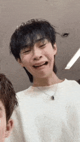 a young man wearing a white shirt and a black necklace makes a funny face