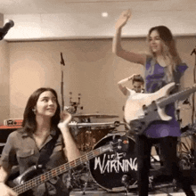 a woman playing a guitar in front of a drum with the word warning on it