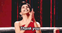 a woman in a red dress is saying thank you with her hands in the air .