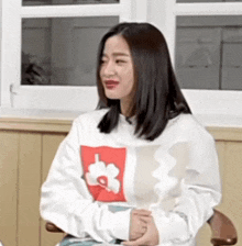 a woman wearing a white sweater with a red flower on it is sitting in a chair .