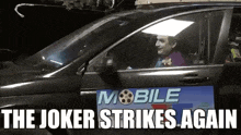a man dressed as the joker is driving a car with the words `` the joker strikes again '' written on the side .