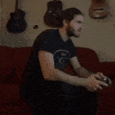 a man in a blue shirt is sitting on a red couch playing a video game