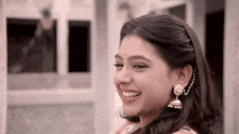 a woman wearing earrings and a headband smiles for the camera