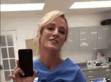 a woman in a blue scrub top is taking a selfie with her cell phone .