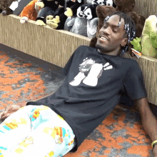 a man wearing a black shirt with a picture of a dog on it is laying on the floor in front of stuffed animals