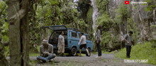 a group of people standing around a blue van with the word terbaik on the bottom right