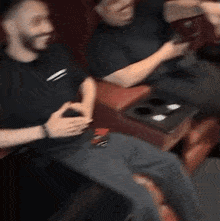 two men are sitting in a movie theater watching a movie and one of them is holding a cell phone .