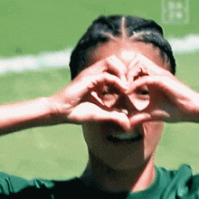 a woman in a green shirt making a heart shape with her hands