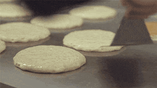 a person is using a spatula to spread batter on a pan of pancakes
