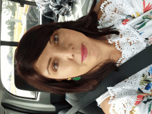 a woman wearing a white lace top and green earrings is sitting in a car