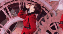 a man in a red jacket stands in front of a clock with roman numerals vii and xii