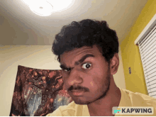 a man is making a funny face in front of a tapestry that says kapwing on it