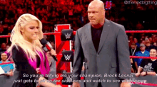 a man in a suit and a woman in a pink dress are standing in a wrestling ring .
