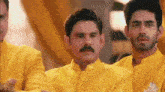 a man with a mustache is standing next to two other men in yellow suits .
