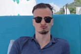 a man wearing sunglasses and a blue shirt is making a funny face .