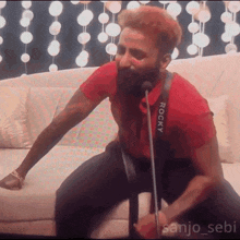 a man wearing a red shirt that says rocky on it is singing into a microphone