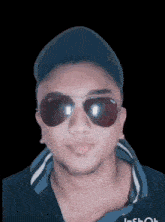 a man wearing sunglasses and a baseball cap looks at the camera with a black background