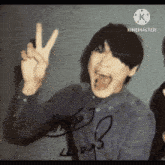 a man in a blue shirt is giving a peace sign and has a signature on his shirt