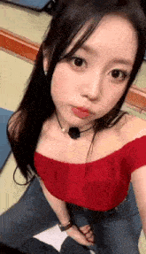 the girl is wearing a red off the shoulder top and jeans and taking a selfie .