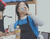 a woman in an apron drinks from a can next to a bottle of sprite