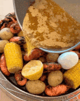 a bucket filled with shrimp corn potatoes and lemons is being poured with sauce